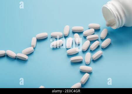 Vitamine und Mineralstoffe in weißen Kapseln fielen aus einem weißen Glas auf blauem Hintergrund. Das Konzept des Immunschutzes, antivirale Prävention. Zusatzfutter Stockfoto