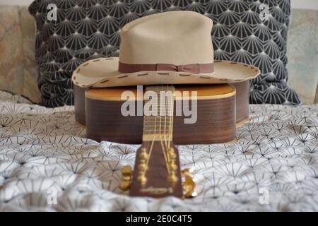 Akustische Volksgitarre und Cowboyhut auf dem Bett Stockfoto