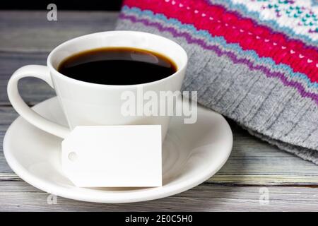 Eine Tasse Kaffee und ein weißes Papieretikett mit Platz für Text auf einem hellen Holztisch. Stockfoto