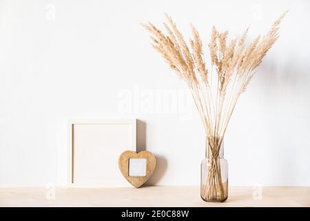 Getrocknete Blumen und ein Fotodramen rammen gegen eine helle Wand hinein Ein minimalistischer Stil Stockfoto