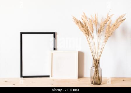 Getrocknete Blumen und ein Fotodramen rammen gegen eine helle Wand hinein Ein minimalistischer Stil Stockfoto