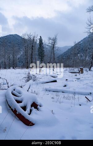 Ein altes Waggonrad, das in der Dämmerung im Schnee begraben liegt, am unteren Ende des Rock Creek, im Missoula County, Montana. Stockfoto