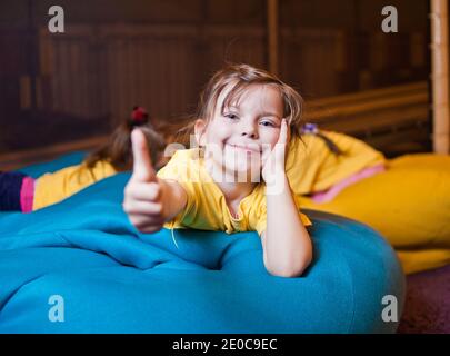 Kleine Mädchen liegen auf der Stuhltasche und zeigen Daumen hoch im Kinderzentrum Stockfoto