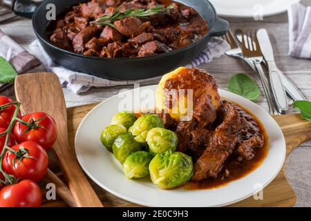 Deutsches Schweinegulasch mit rosenkohl und Kartoffelknödeln Eine Platte Stockfoto