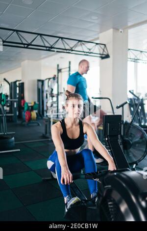 Funktionales Trainingskonzept. Sport Mann und Frau tun Übung im Simulator Rudergerät und Air Bike im Fitnessstudio Stockfoto