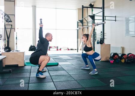 Paarschulung. Sport Frau und Mann heben die leere Bar der Bar über den Kopf und schauen sich gegenseitig in der Turnhalle Stockfoto