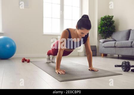 Fröhliche junge Frau tun volle Planke auf Sportmatte während Fitnesstraining zu Hause Stockfoto