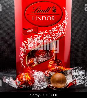 Nahaufnahme einer aufrechten roten Schachtel mit Lindt Lindor umhüllten Schokoladentrüffeln, einige davon im Fenster der Schachtel und zwei Schokoladen draußen. Stockfoto