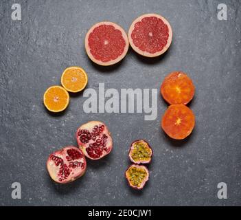 Draufsicht auf Pomegrade, Orange, Grapefruit, Passionsfrucht und Kaki auf dunkelgrauem Steinhintergrund, paarweise angeordnet. Gesunde und frische Früchte Stockfoto
