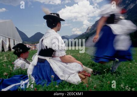 Deutschland /Bayern / Bayerisches Fest /Ein Coupel sitzt in traditioneller Kleidung im Gras und ein junges Mädchen kommt verschwommen vorbei Stockfoto