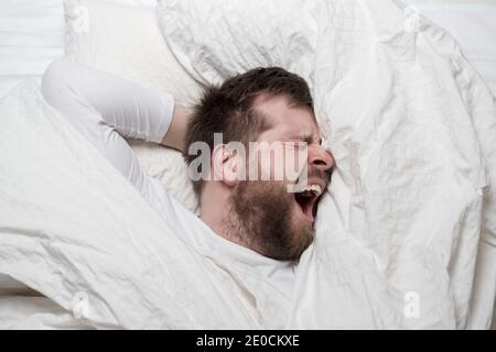 Schlaflosigkeit. Der junge Mann kann nicht schlafen, er steht unter Stress, leidet und schreit. Konzept der psychischen Gesundheit. Stockfoto