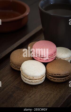 Eine Nahaufnahme von köstlichen süßen Macarons mit einem heißen tasse Kaffee auf einem hölzernen Hintergrund für eine gemütliche Snack oder Leckerbissen Stockfoto