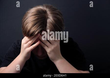 Teenager sitzt in einer geschlossenen Haltung mit psychischen Problemen Wie z. B. Depression während der COVID-19-Sperre Stockfoto