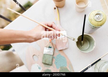 Draufsicht auf eine nicht erkennbare Frau, die Pinsel in der Nähe verschiedener Farben hält und Pinsel auf dem Tisch in der kreativen Werkstatt platziert Stockfoto