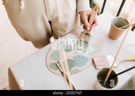 Von oben von unkenntlich Ernte weibliche Maler mit Pinsel und Farbpalette Mischung verschiedener Farben während der Arbeit in hellen Werkstatt Stockfoto