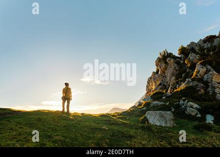 Rückansicht des nicht erkennbaren Reisenden auf grünem Hügel und stehen Bewundern Sie die malerische Aussicht auf den Sonnenuntergang Himmel im Hochland Stockfoto