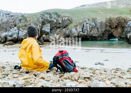 Rückansicht von nicht erkennbaren Entdecker mit Rucksack entspannend auf steinigen Küste von Cobijero Beach und bewundernde erstaunliche Aussicht auf den See An bewölktem Tag in autu Stockfoto