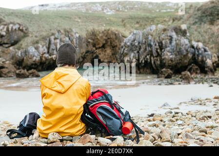 Rückansicht von nicht erkennbaren Entdecker mit Rucksack entspannend auf steinigen Küste von Cobijero Beach und bewundernde erstaunliche Aussicht auf den See An bewölktem Tag in autu Stockfoto