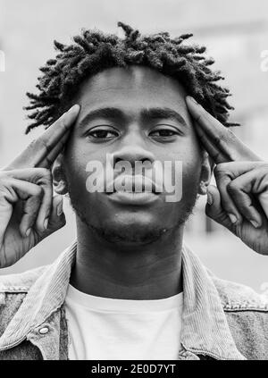 Schwarz und weiß von ernsten jungen afroamerikanischen Hipster männlich Mit Afro Frisur berühren Tempel und Blick auf die Kamera Stockfoto