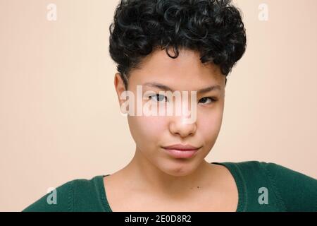 Junge Latina-Frau, die mit ihren asiatischen Augen auf die Kamera schaut, isoliertes horizontales Foto, beigefarbener Hintergrund Stockfoto