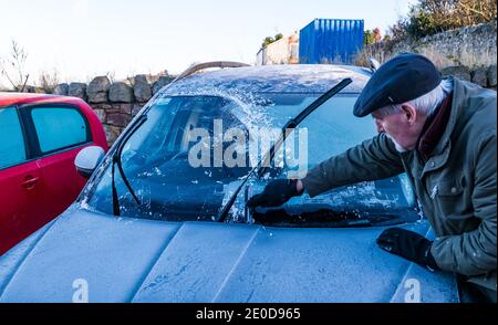 Senior man kratzt Eis von der Windschutzscheibe im Winter mit Frostmustern auf dem Autodach, Schottland, Großbritannien Stockfoto