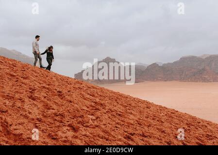 Seitenansicht von ein paar Reisenden, die den sandigen Hügel hinunterlaufen Im Wadi Rum Sandsteintal, während Sie Freiheit und Urlaub genießen In Jordanien Stockfoto