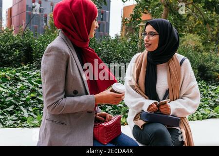 Freundliche arabische Freundinnen sitzen auf der Straße und reden mit Sich gegenseitig, während wir das Wochenende zusammen genießen Stockfoto