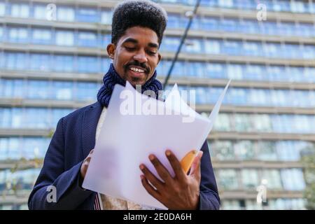 Niedriger Winkel der lächelnden afroamerikanischen männlichen Unternehmer stehen in Innenstadt und Lesen von Dokumenten Stockfoto