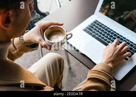 Von oben Ernte anonymen männlichen Unternehmer sitzt im Café mit tasse Kaffee und Tippen auf Netbook während der Arbeit an Projekt online Stockfoto