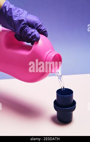 Crop anonyme Person mit Plastikflasche Gießen Flüssigwaschmittel in Kappe auf Tisch im Studio platziert Stockfoto
