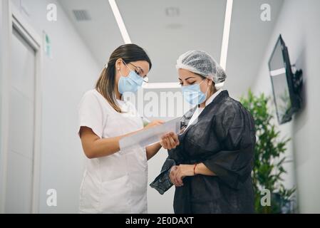 Weibliche Kosmetologen stehen im Korridor der Schönheitsklinik und sprechen Info zum Client während der Notizen in der Zwischenablage Stockfoto