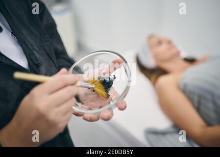 Crop Dermatologe mit schwarzen kosmetischen Maske in Schüssel Vorbereitung für Hautpflegeverfahren im Schönheitssalon Stockfoto