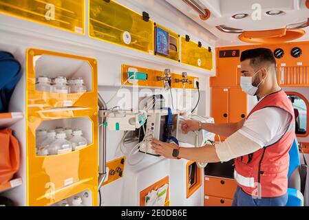 Seitenansicht des männlichen Sanitäter in Maske mit elektronischer Medizin Ausrüstung in modernen Ambulanzwagen Stockfoto