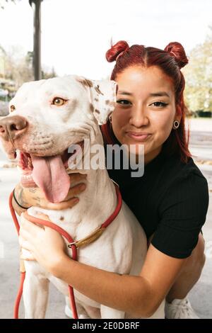 Lächelnd junge asiatische weibliche Besitzer umarmt gehorsam reinrassige American Pit Bull Terrier Hund und Blick auf die Kamera Stockfoto