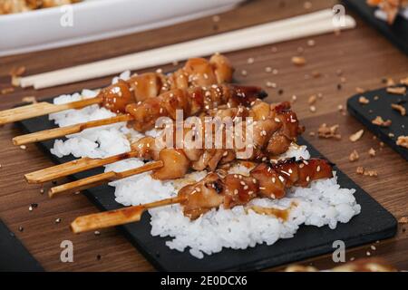 Hühnersatay mit weißem Reis auf Schiefertablett angeordnet Holztisch im Restaurant Stockfoto