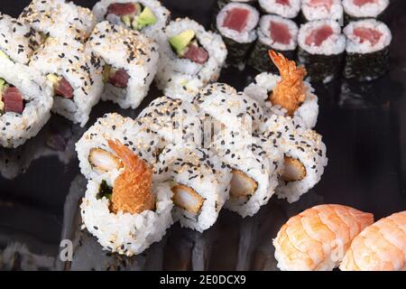 Verschiedene leckere Brötchen und Sushi auf schwarzem Teller Stockfoto