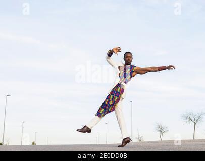 Seitenansicht des afroamerikanischen Tänzers im trendigen Outfit Durchführung energischer Bewegungen gegen blauen Himmel Stockfoto