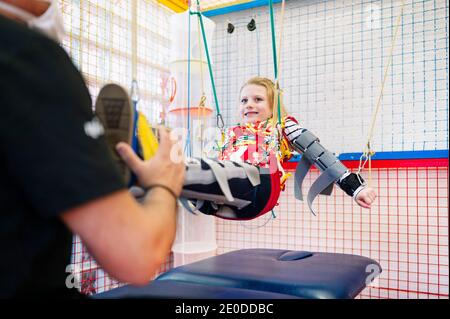 Crop anonyme Spezialist Unterstützung für Mädchen mit Angelman-Syndrom Während des Rehabilitationstrainings mit elastischen Bändern Stockfoto