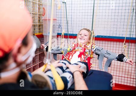 Crop anonyme Spezialist Unterstützung für Mädchen mit Angelman-Syndrom Während des Rehabilitationstrainings mit elastischen Bändern Stockfoto