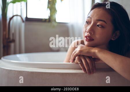 Fröhliche junge asiatische Frau, die in der Badewanne in einem Hotelzimmer mit traditionellem orientalischem Dekor baden kann, während sie ihren Urlaub in Taiwan verbringt Stockfoto