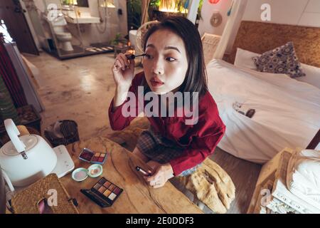 Junge asiatische weibliche Blick auf Reflexion im Spiegel und Anwendung mascara während des täglichen Make-up am Morgen Stockfoto