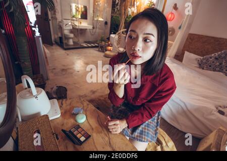 Junge asiatische weibliche Anwendung roten Lippenstift, während im Vordergrund stehen Spiegel im Zimmer mit traditionellem orientalischen Interieur Stockfoto