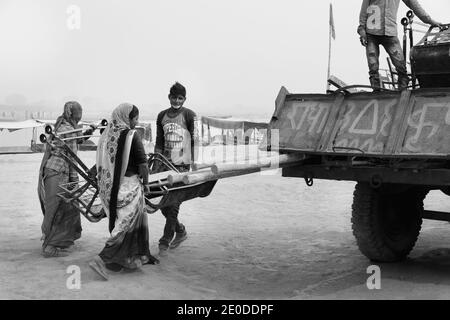 Frauen und Mann laden am heißen Sommertag am Fluss Yamuna in Vrindavan, Uttar Pradesh, Indien, zerlegte Stühle mit großem Rad auf einen wartenden Lastwagen. Stockfoto