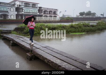 Frau mit Regenschirm, die entlang einer hölzernen Fußgängerbrücke geht und dabei die Einsamkeit genießt An regnerischen Tag in Yilan County und wegschauen Stockfoto