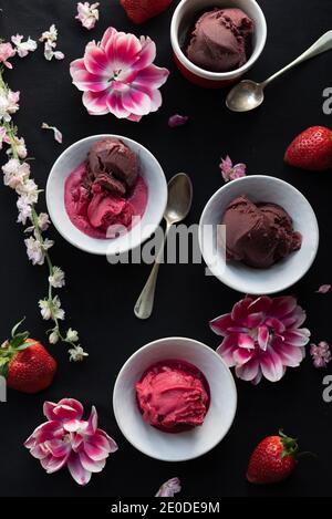 Von oben von Erdbeere und Schokolade Eisschaufeln angeordnet Auf schwarzem Hintergrund mit Blumen und Beeren Stockfoto