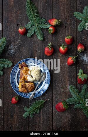 Von oben ein köstliches Dessert mit einer Kugel Eis Auf Teller auf Tisch mit Erdbeeren und trockenem Ahorn gelegt Blätter Stockfoto