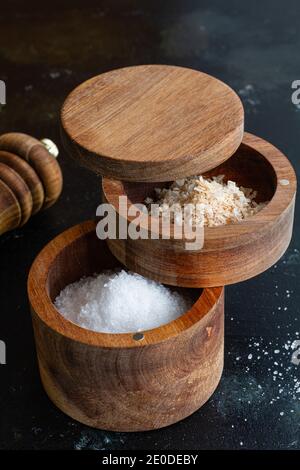 Hoher Winkel von verschiedenen Arten von Salz in Holzkrügen Platziert auf Tisch mit Pfeffermühle in der Küche Stockfoto