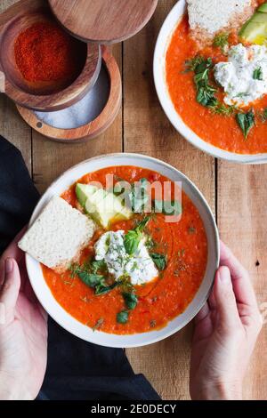 Draufsicht auf Ernte anonyme Person mit Anteil der hausgemachten Tomatensuppe in Schüssel auf Holztisch gelegt Stockfoto