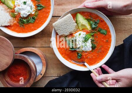 Draufsicht auf Ernte anonyme Person mit Anteil der hausgemachten Tomatensuppe in Schüssel auf Holztisch gelegt Stockfoto