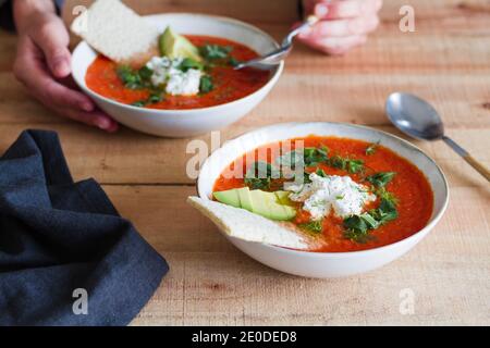 Crop anonyme Person mit Teil der hausgemachten Tomatensuppe in Schüssel auf Holztisch platziert Stockfoto